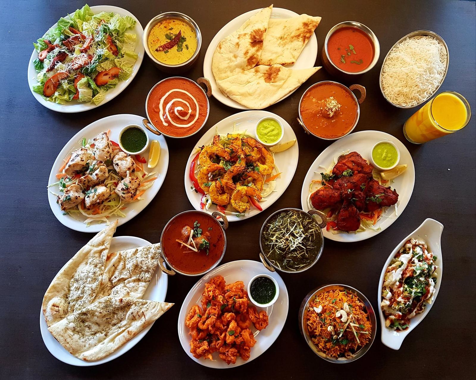A table spread of Spice Valley dishes: butter chicken, tandoori chicken, prawns, naan, biryani and curries